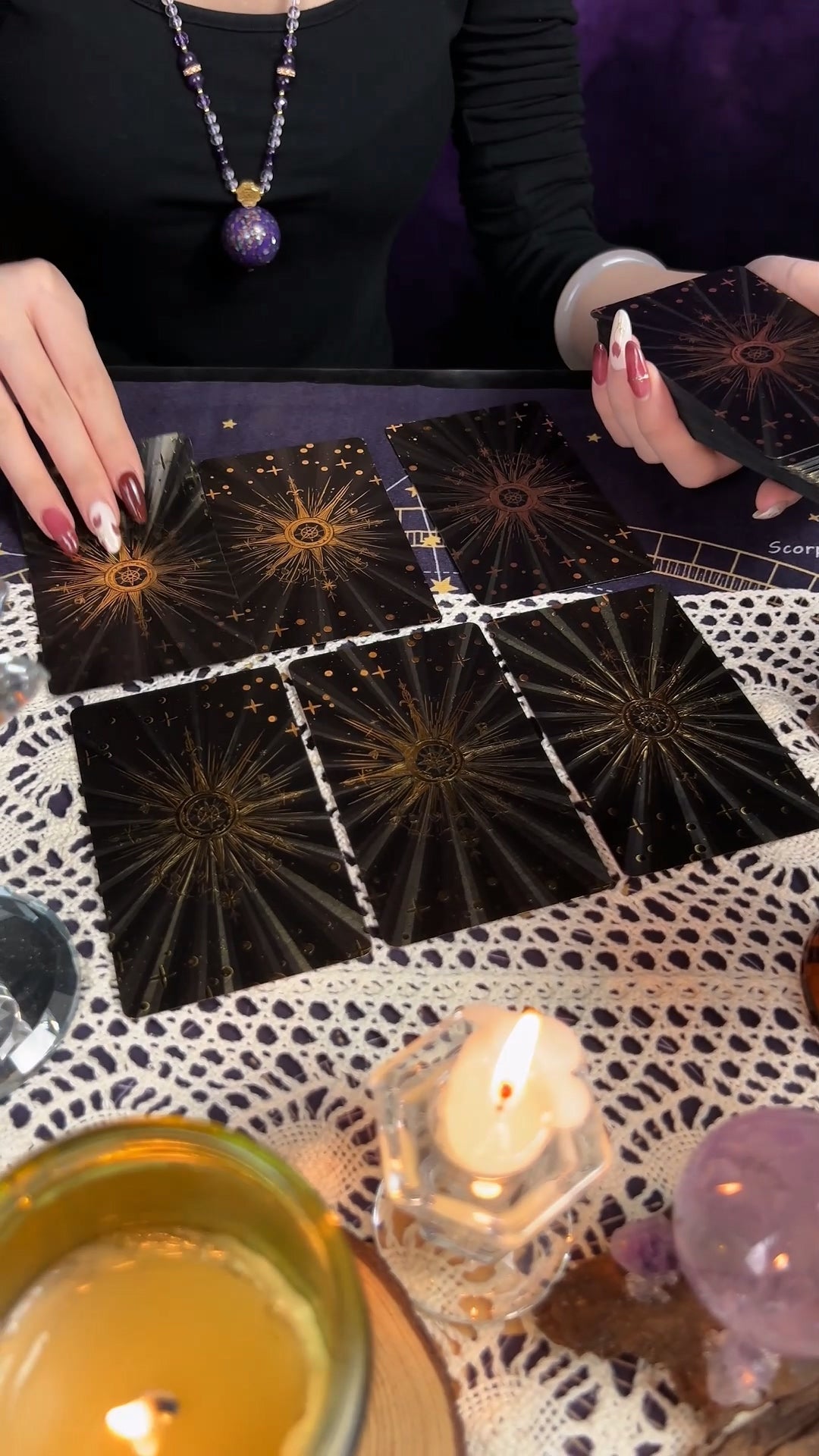 Hands laying tarot cards on a dark cloth beside a candle
