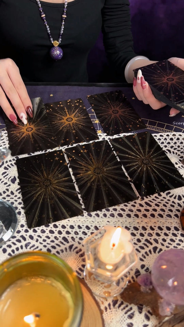Hands laying tarot cards on a dark cloth beside a candle